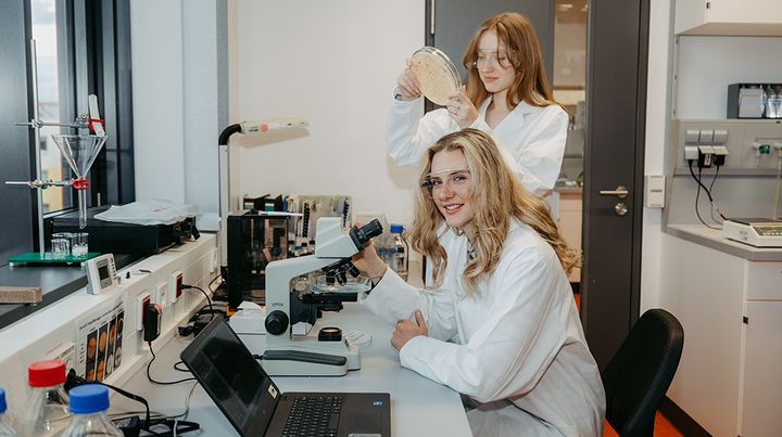 2 Studentinnen im Labor, die eine an einem Mikroskop, die andere hat eine Probe in der Hand (c) Jana Dünnhaupt Uni Magdeburg